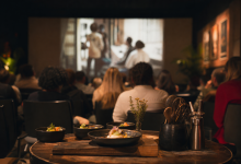 Público acompanha sessão de cinema em espaço cultural com mesa de degustação em primeiro plano