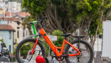 Bicicletas elétricas estacionadas ao ar livre, com árvores ao fundo.