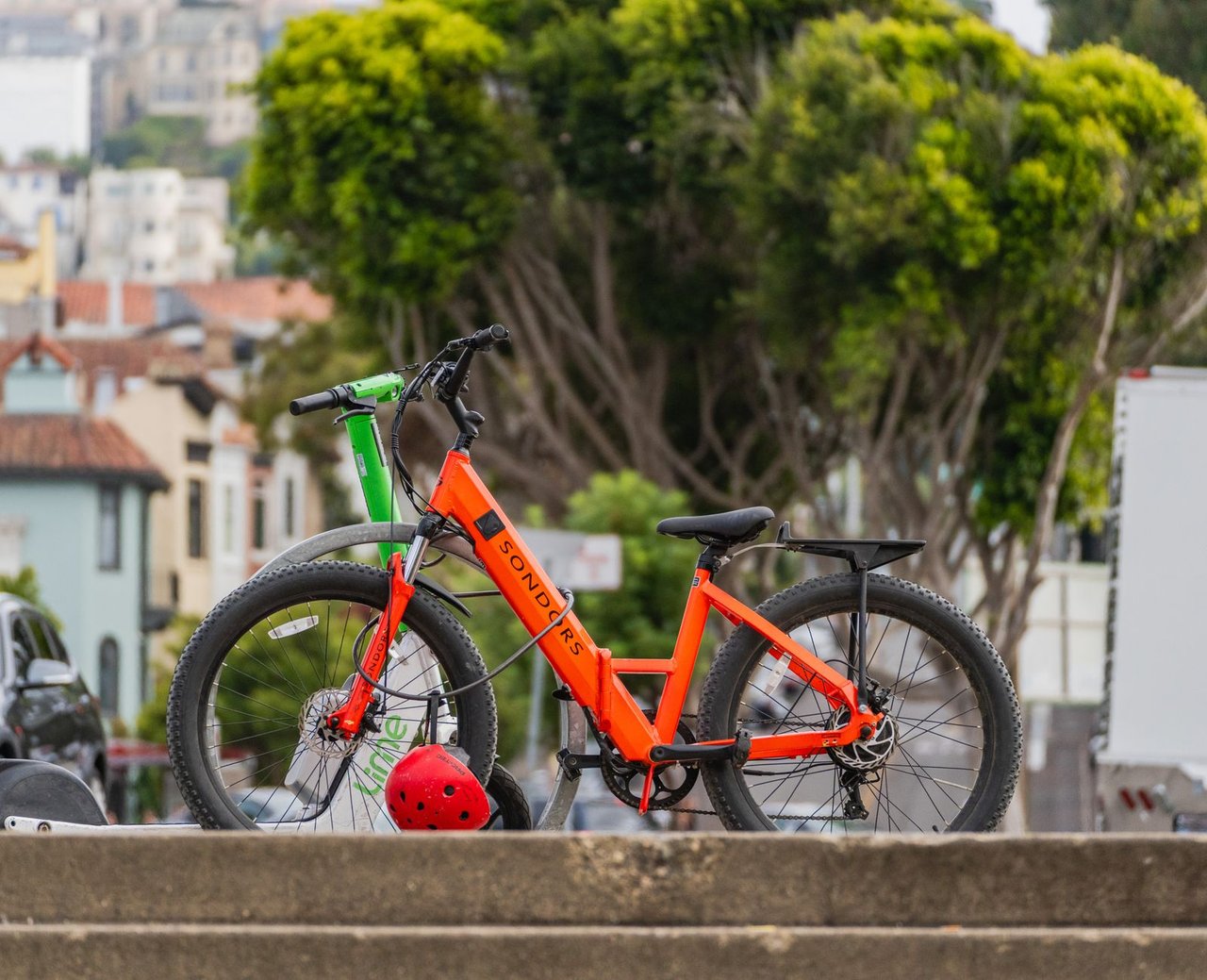 Bicicletas elétricas estacionadas ao ar livre, com árvores ao fundo.