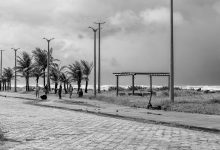 Calçadão da orla de Peruíbe, com palmeiras e o mar ao fundo, sob céu nublado.