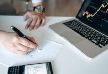 Mãos analisam dados financeiros em uma mesa com notebook e calculadora.