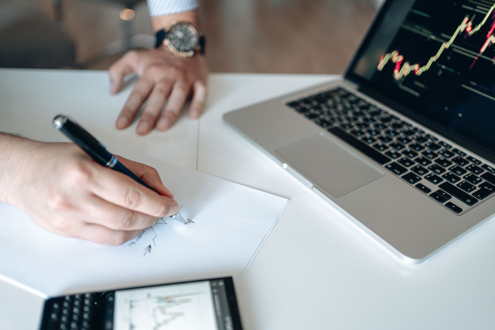 Mãos analisam dados financeiros em uma mesa com notebook e calculadora.