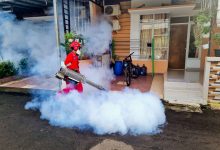 Agente de controle de pragas usa uma máquina de fumaça para pulverizar a área externa de uma residência.