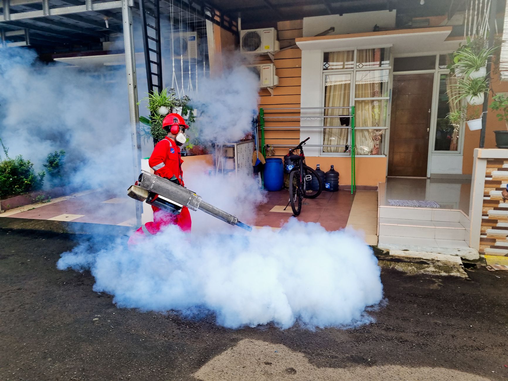 Agente de controle de pragas usa uma máquina de fumaça para pulverizar a área externa de uma residência.